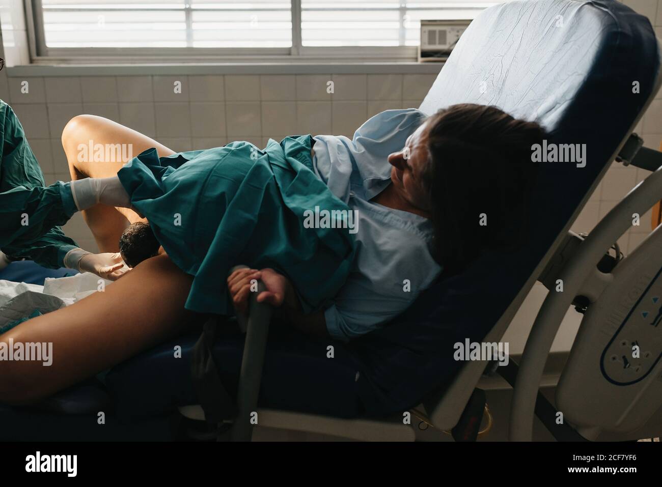 Impugnatura di presa femminile tesa e grunting nel dolore mentre dà nascita al bambino su sedia medica in ospedale moderno Foto Stock