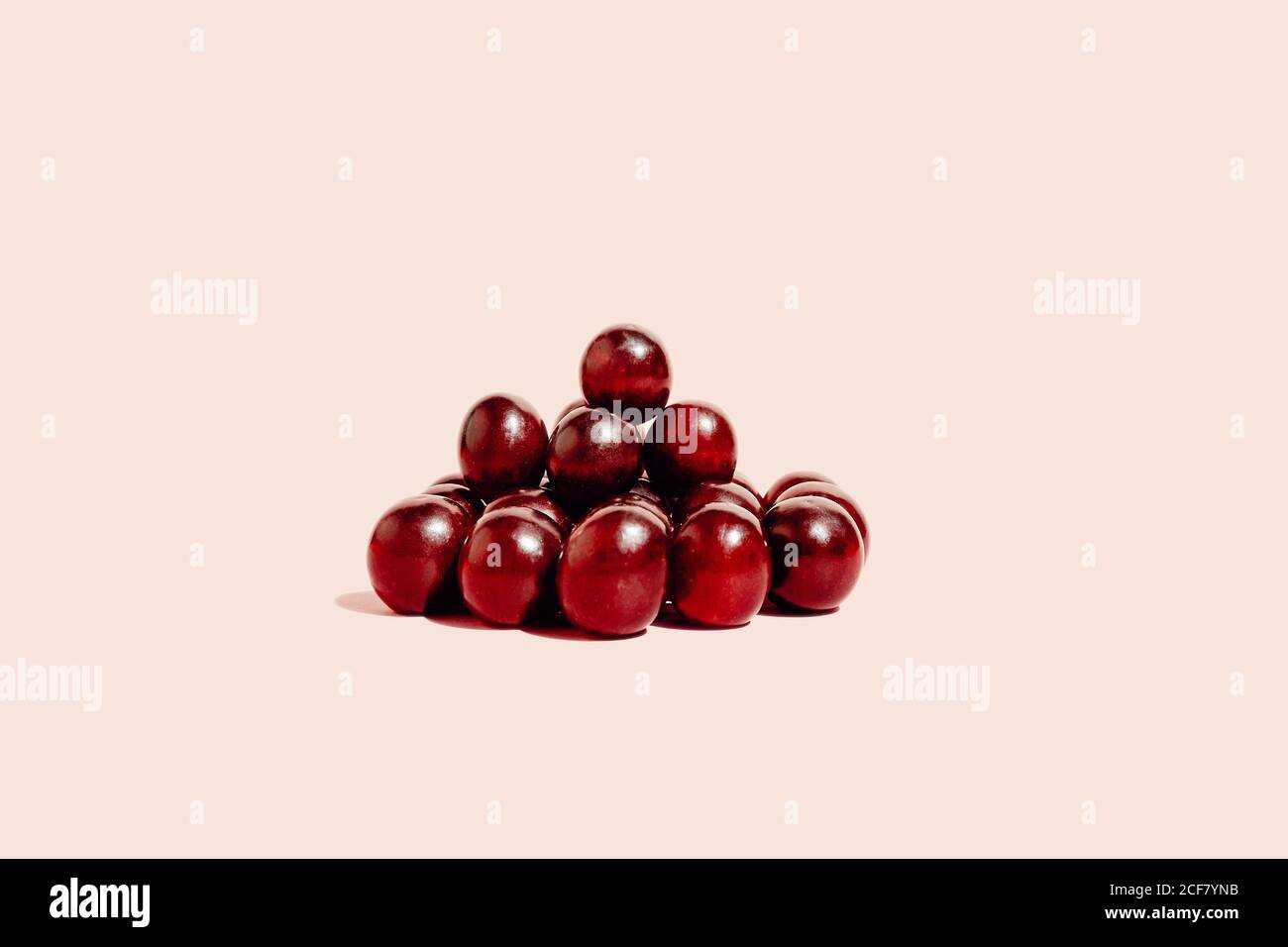 Pila di uve rosse fresche disposte su superficie rosa in studio Foto Stock