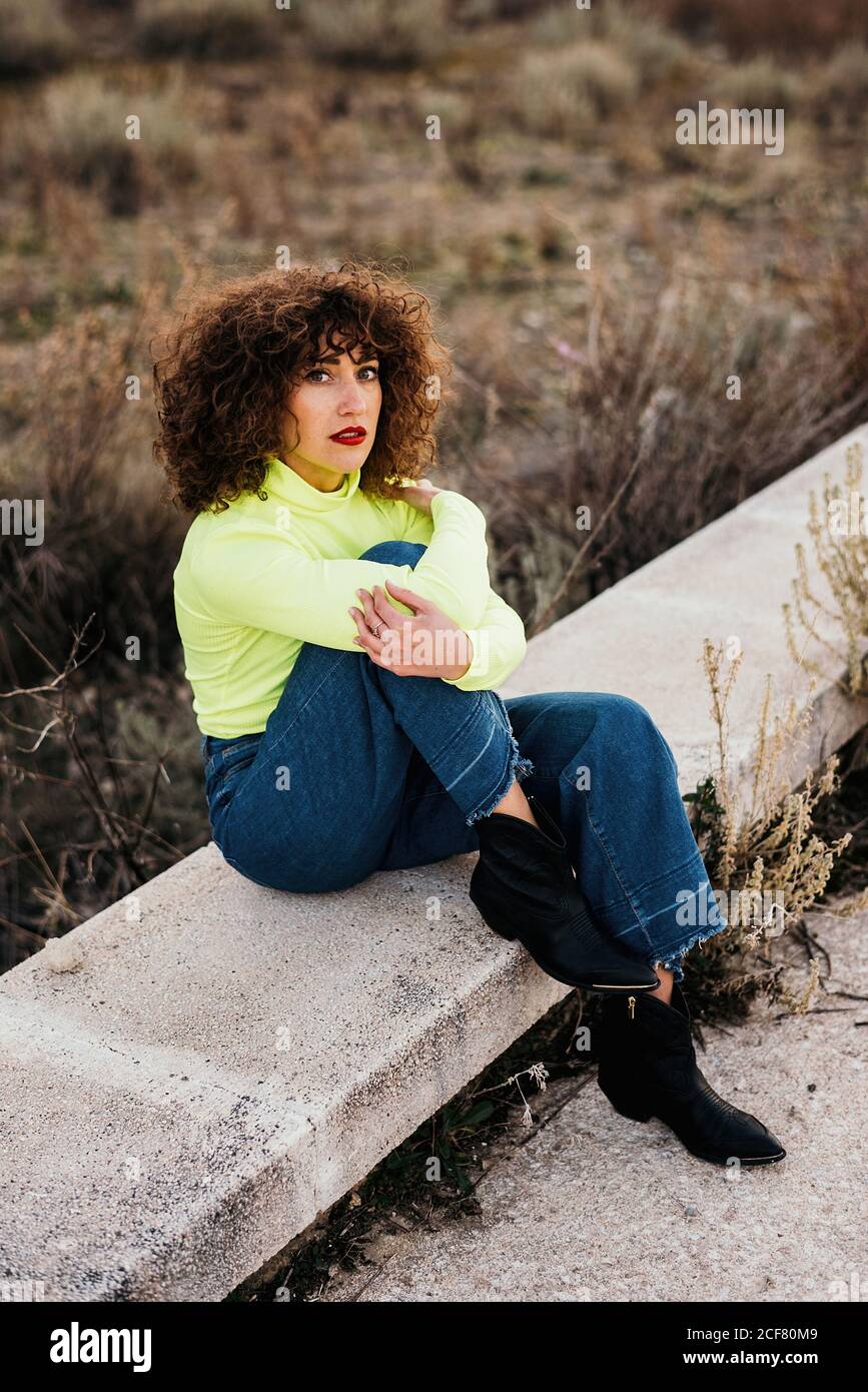Dall'alto del modello femminile giovane in un abbigliamento casual alla  moda e gli occhiali con le labbra rosse che si siedono sulla pietra e che  guardano alla telecamera Foto stock - Alamy