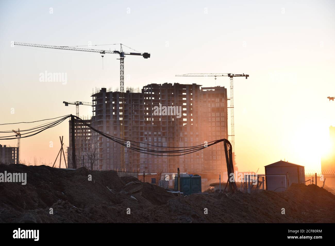 Sagome di gru a torre che costruiscono un nuovo edificio residenziale in un cantiere di costruzione sullo sfondo del tramonto. Programma di ristrutturazione, sviluppo, Foto Stock
