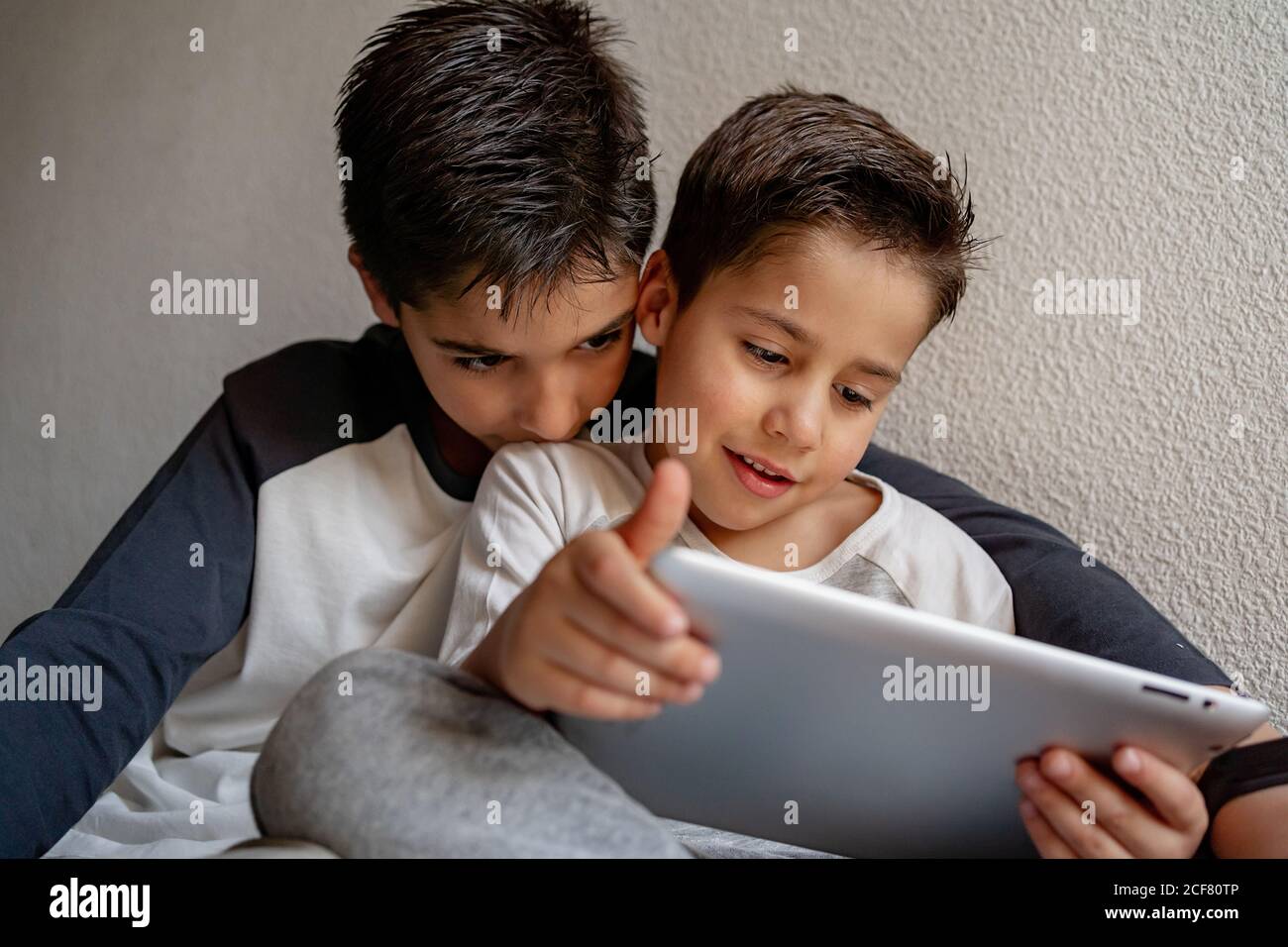 Sorridi i fratelli in dormeuta seduti su un comodo letto e guardando film insieme mentre si divertono a casa Foto Stock