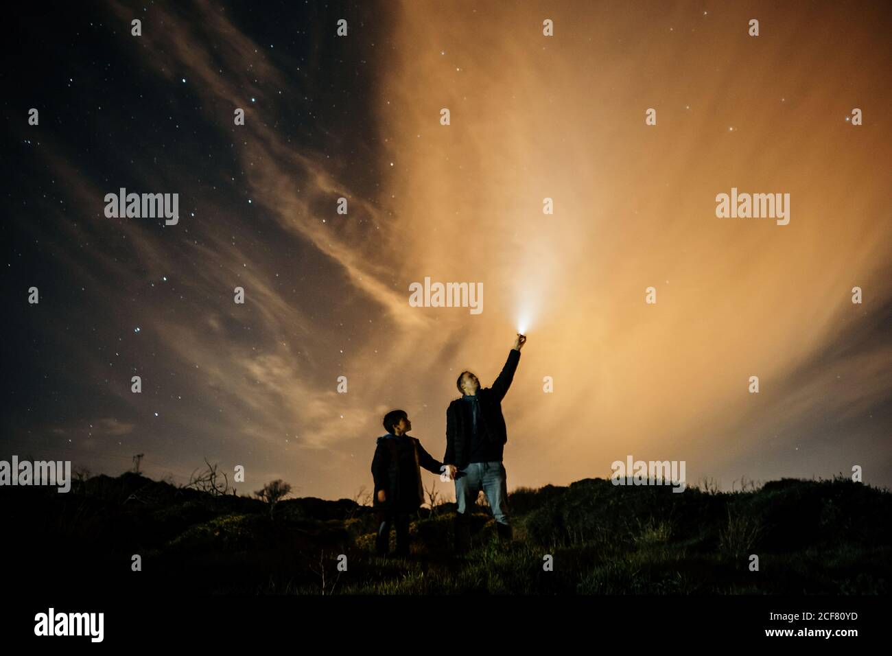 Dad e figlio spensierati che tengono le mani e osservano il cielo stellato mentre si guarda e si illumina con la torcia di notte Foto Stock