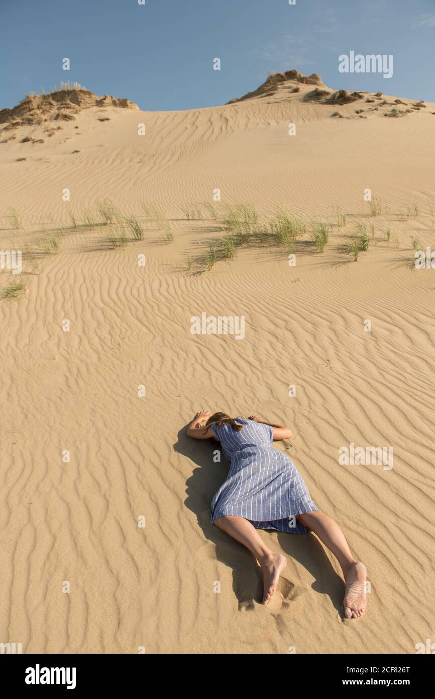 Vista laterale della giovane donna in abito casual sdraiato con faccia in giù sulla duna di sabbia nel caldo giorno d'estate Foto Stock