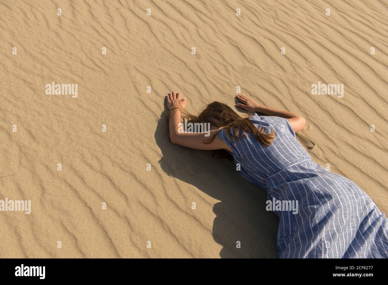 Vista laterale della giovane donna in abito casual sdraiato con faccia in giù sulla duna di sabbia nel caldo giorno d'estate Foto Stock