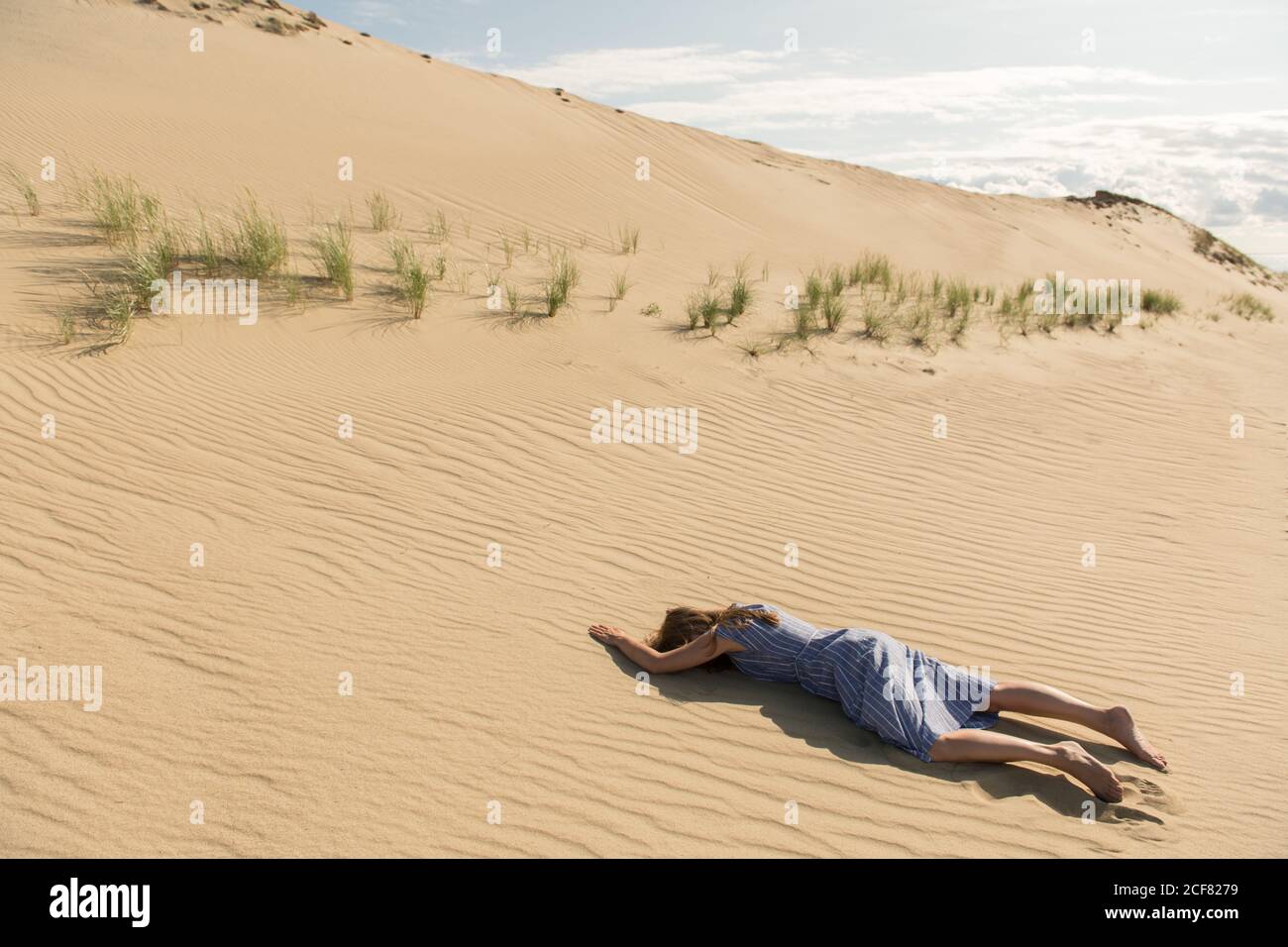 Vista laterale della giovane donna in abito casual sdraiato con faccia in giù sulla duna di sabbia nel caldo giorno d'estate Foto Stock