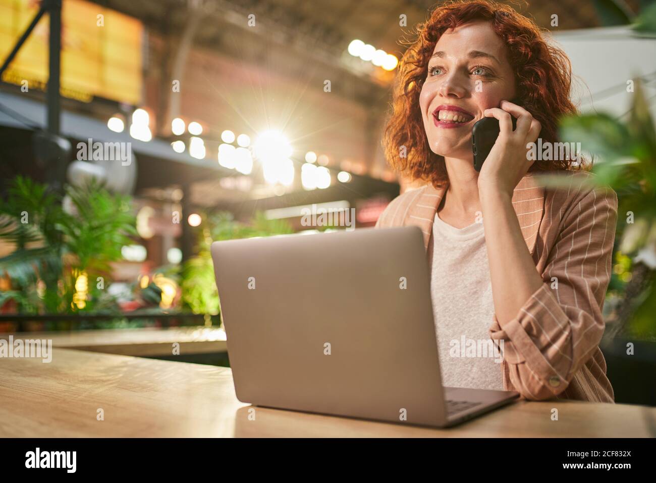 Giovane donna che parla al telefono mentre lavora sul computer portatile Foto Stock