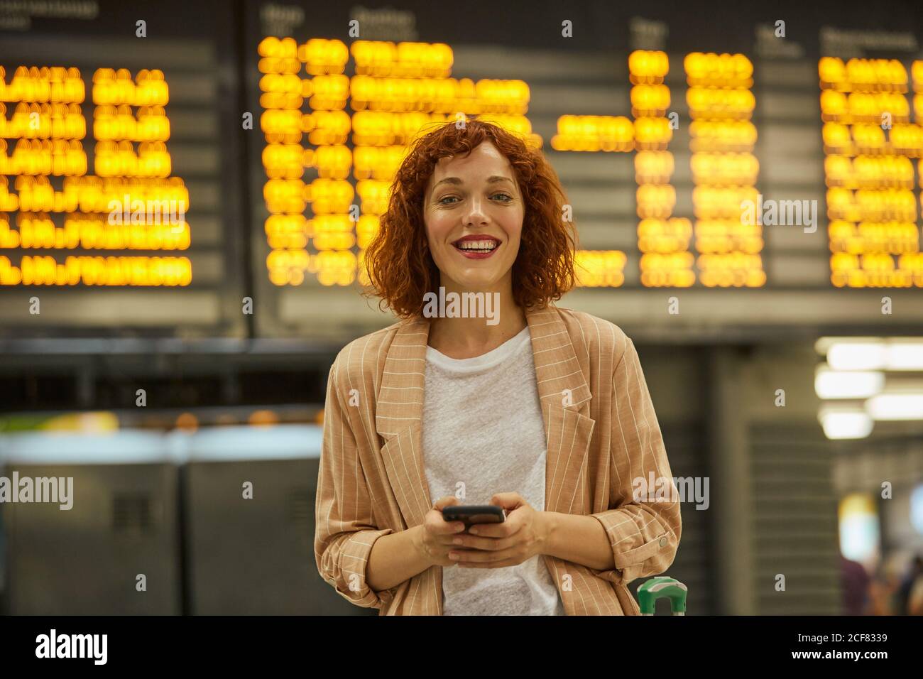Giovane donna dai capelli rossi che usa lo smartphone alla stazione Foto Stock