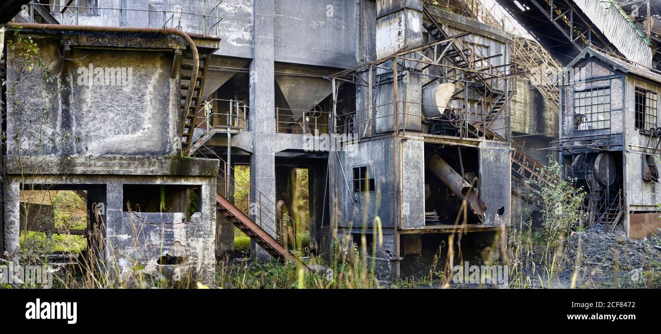 Cemento grigio edifici industriali dilapidati di miniera di carbone abbandonato con varie scale metalliche e tubi che si localizzano su blocchi di carbone Foto Stock