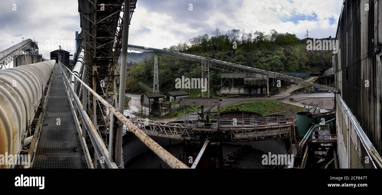 Vecchi edifici industriali disabitati scabdati con carrelli per il trasporto del carbone in campagna che si affaccia sulle montagne verdi sulla miniera di carbone abbandonata giorno nuvoloso Foto Stock