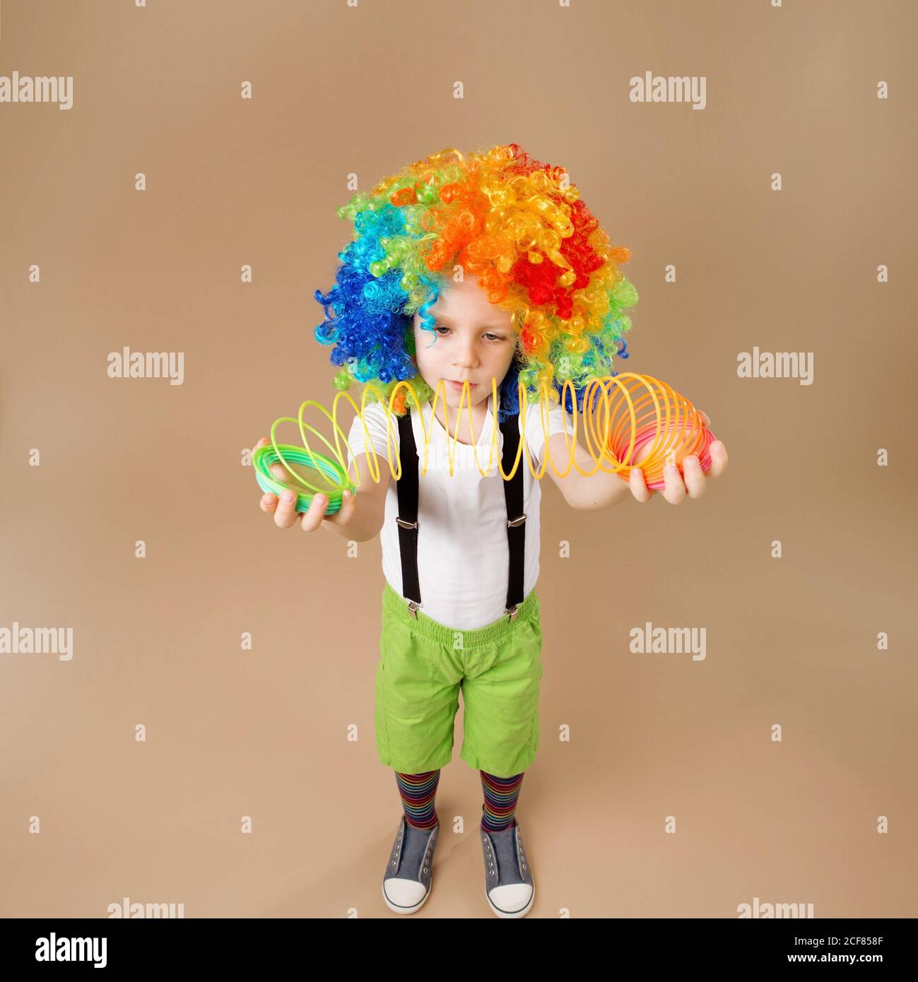 Buon ragazzo clown con grande parrucca colorata. Piccolo ragazzo in parrucca  clown gioca con una primavera. Ritratto di un bambino girato su un  obiettivo grandangolare. Ragazzo di compleanno. Pos Foto stock 