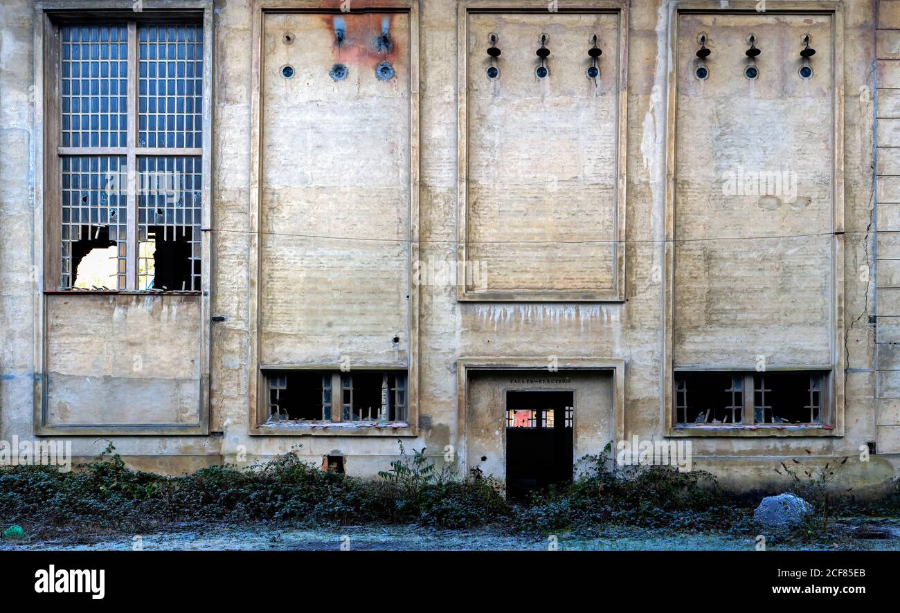 Esterno di un edificio industriale in pietra abbandonato con strette finestre con griglia metallica e vetro rotto Foto Stock
