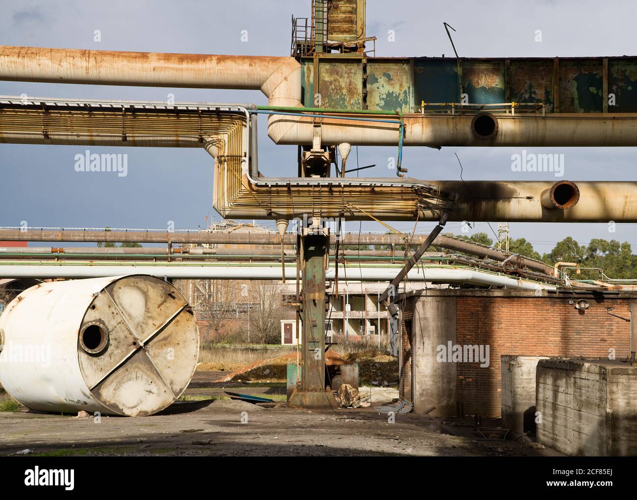 Pipeline arrugginite intemperie su strada sopra l'area industriale abbandonata con grande serbatoio in metallo a terra Foto Stock