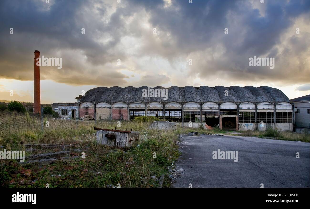 edificio industriale in pietra solitario con pareti grigie in shabby Tra cespugli verdi contro il cielo nuvoloso nelle Asturie in Spagna Foto Stock
