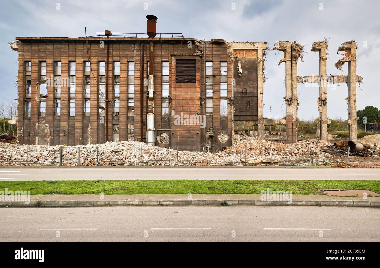 Rovine di vecchia costruzione industriale abbandonata con tubi e pali Di rifiuti situato vicino alla strada contro cielo nuvoloso in Spagna Foto Stock