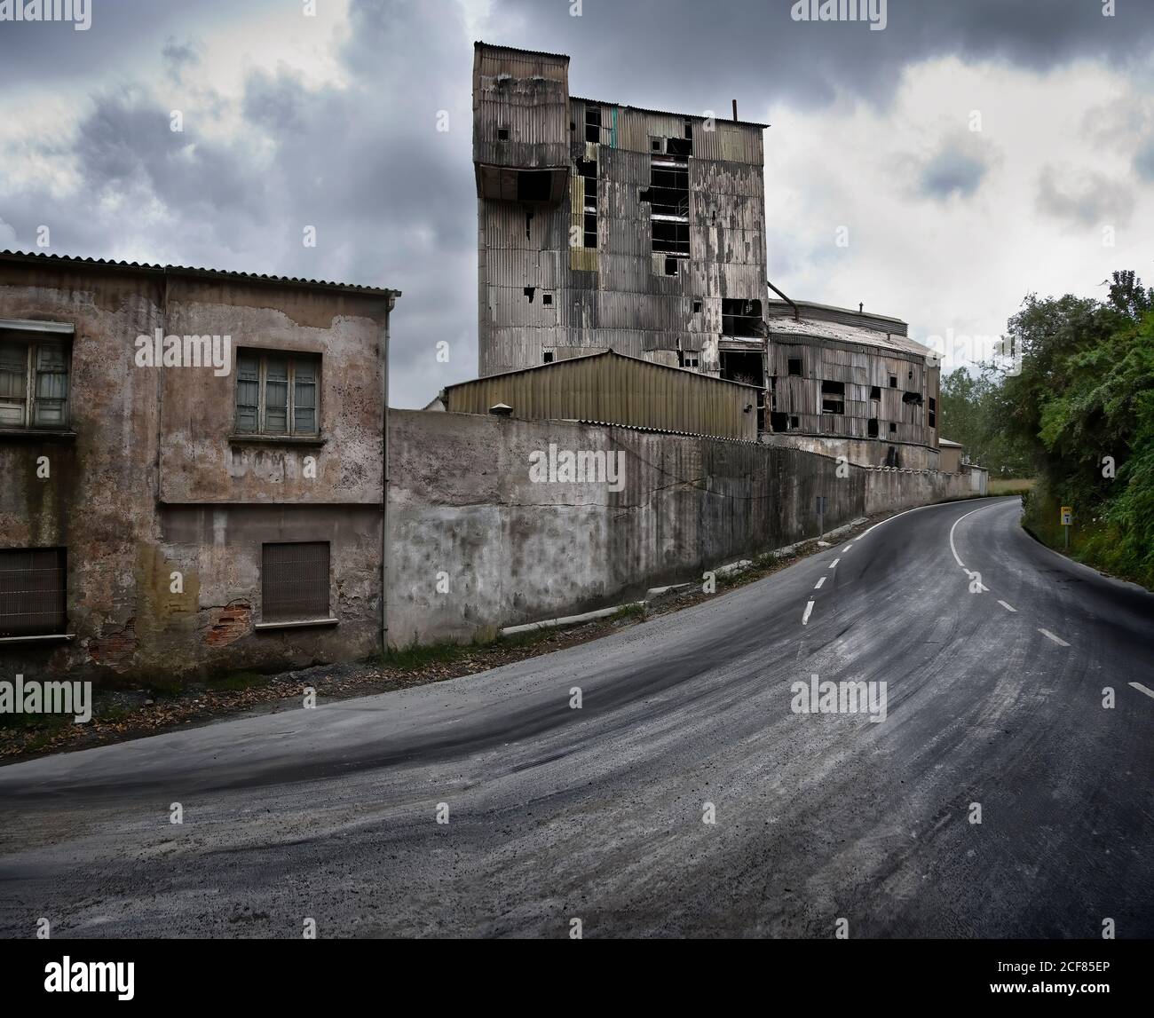 Vecchi edifici industriali trascurati con pareti in pietra intemperie lungo Strada curvilinea in un giorno nuvoloso in Spagna Foto Stock