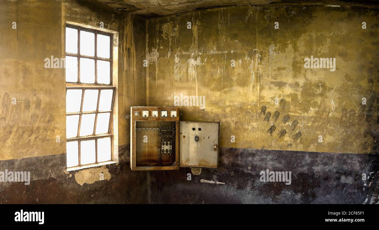 La vecchia scatola di commutazione è installata nell'angolo della stanza con le intemperie pareti in pietra ardesolata e finestra con griglia all'interno industriale desolato edificio Foto Stock