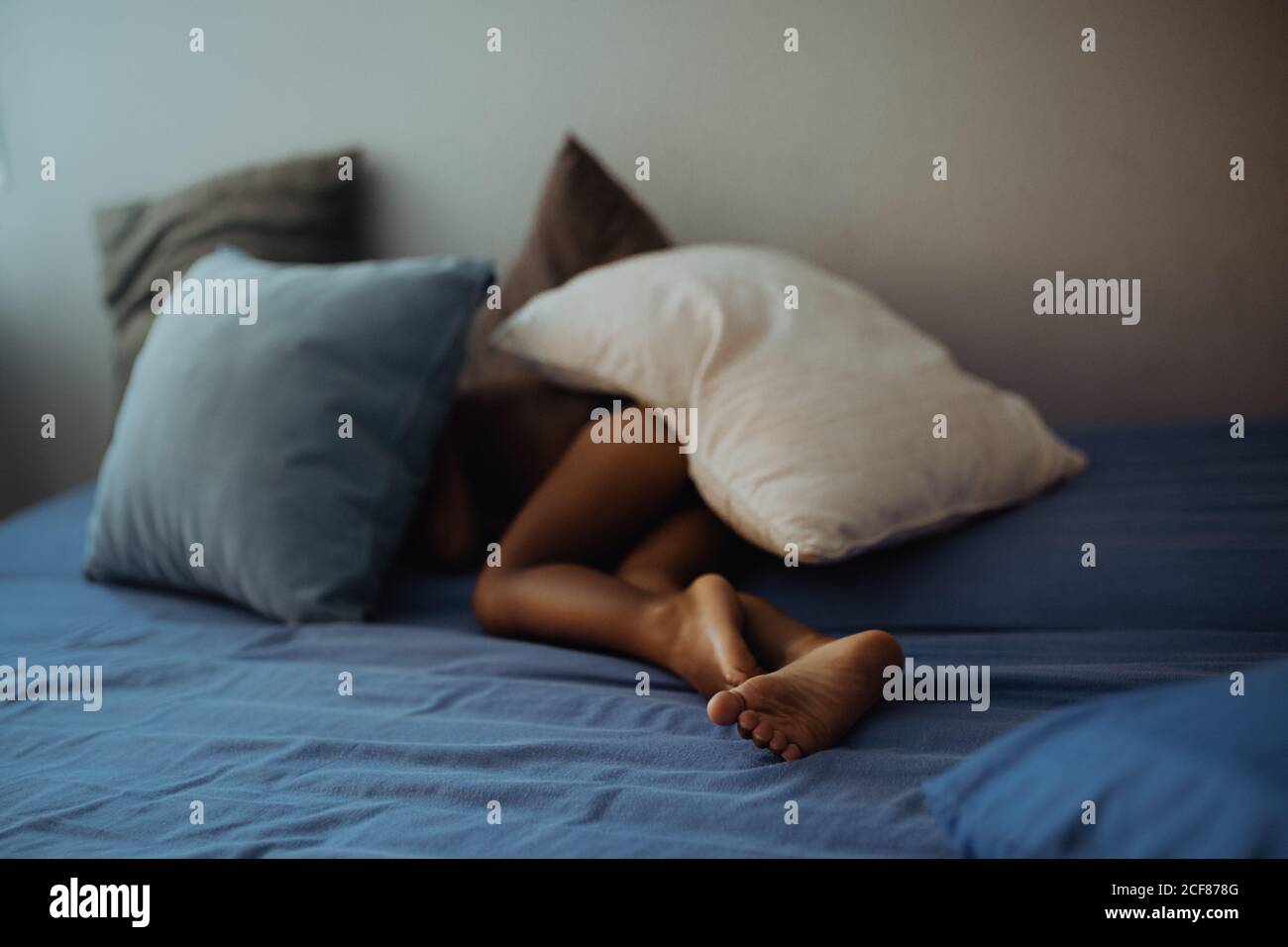bambino irriconoscibile a piedi nudi sdraiato sotto cuscini su un comodo letto dentro camera accogliente Foto Stock