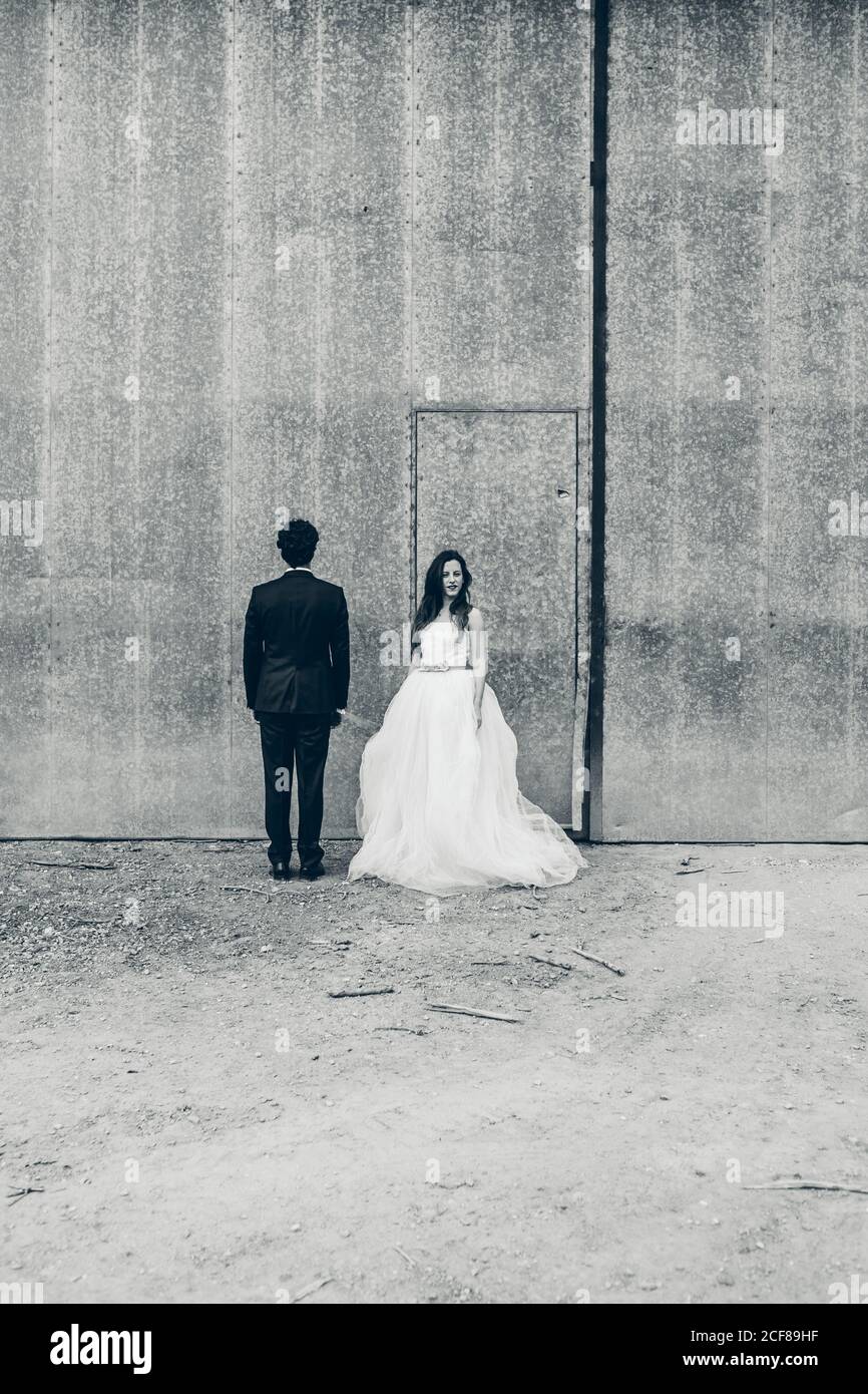 Groom bianco e nero in elegante smoking e sposa abito da sposa bianco in piedi sullo sfondo di un edificio shabby durante giorno di nozze Foto Stock