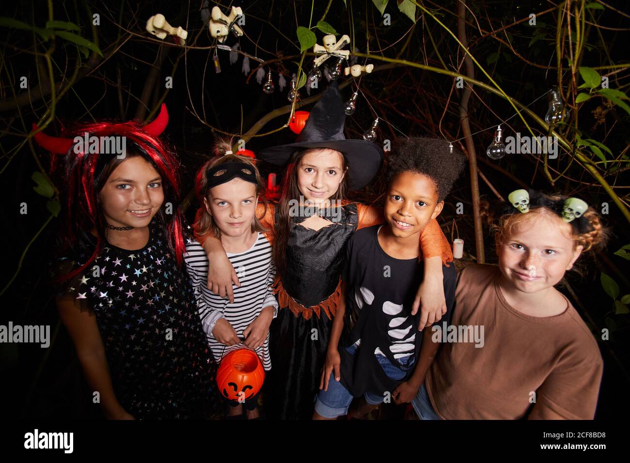 Gruppo di bambini felici in costumi sorridenti a macchina fotografica e. Celebrare Halloween insieme in foresta scura Foto Stock