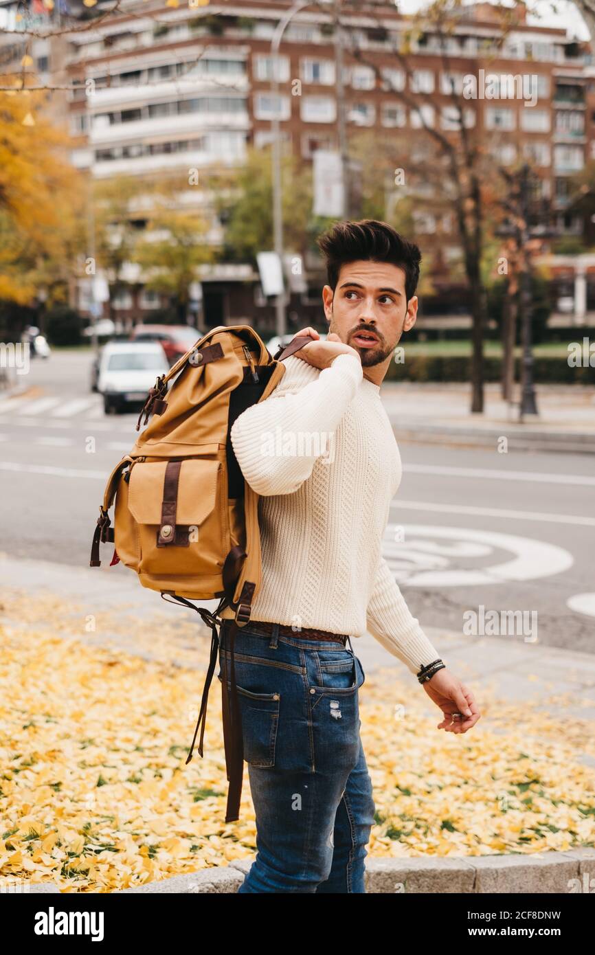 Uomo alla moda in jeans e pullover bianco con zaino arancione a spalla e  guardando via nella città d'autunno Foto stock - Alamy