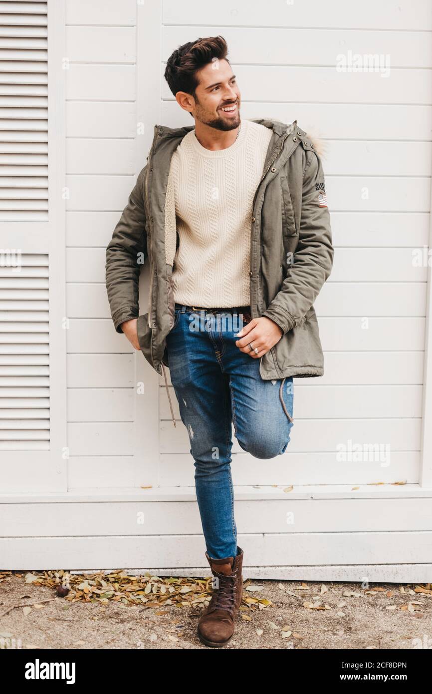 Giovane trendy in jeans, stivali e parka poggiato su una parete bianca e  sorridente all'aperto Foto stock - Alamy