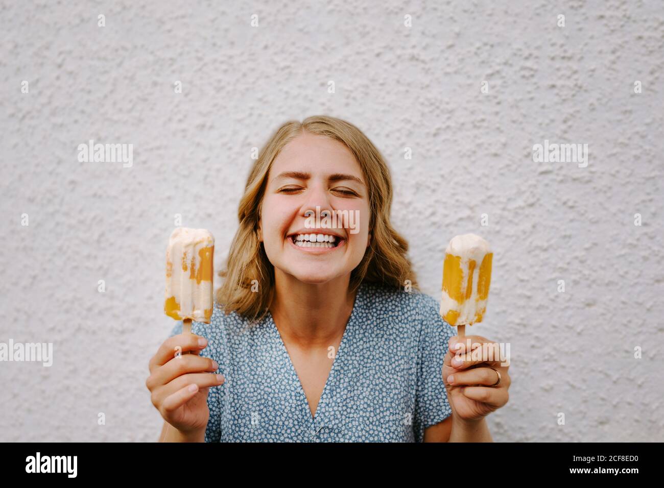 Femmina con gli occhi chiusi facendo simpatici grimace volti con gustoso lecci di ghiaccio su bastoni su sfondo bianco Foto Stock