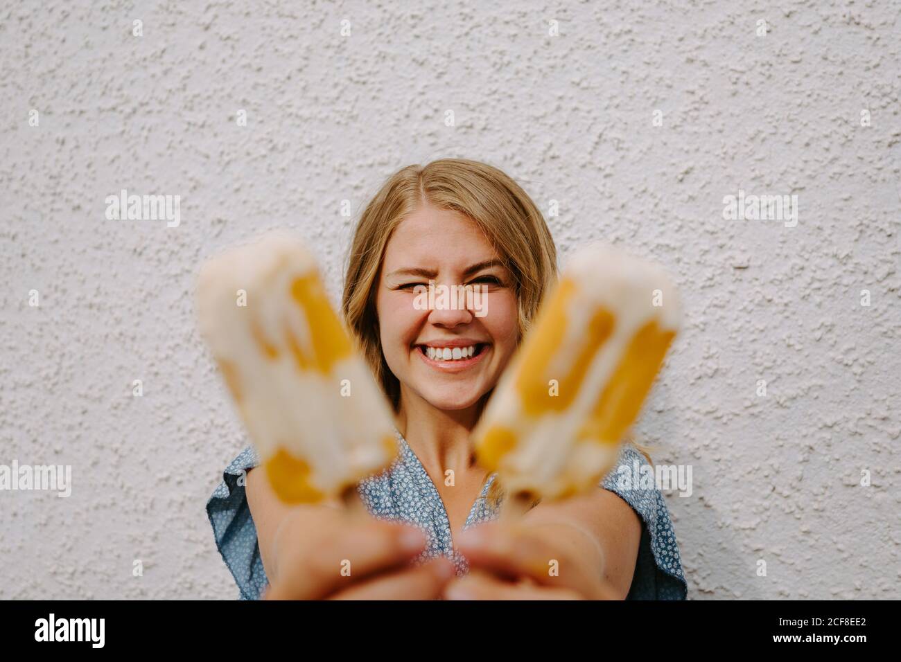 Femmina occhi lampeggianti e rendendo divertente grimace volti con gustoso lecci di ghiaccio su bastoni su sfondo bianco Foto Stock