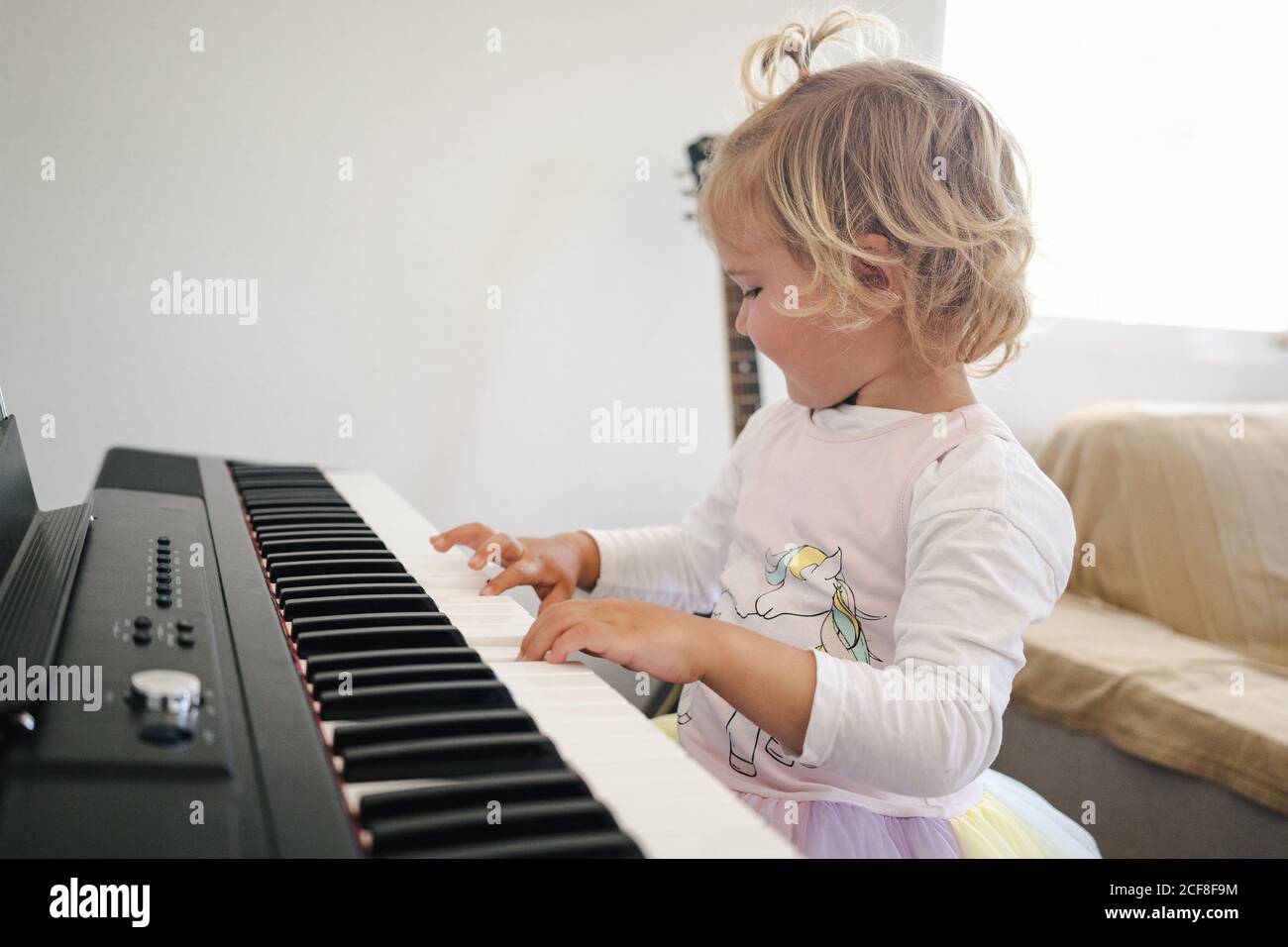 Vista laterale della studentessa in gonna soffice seduta al sintetizzatore e preparandosi per la lezione di musica che guarda via Foto Stock