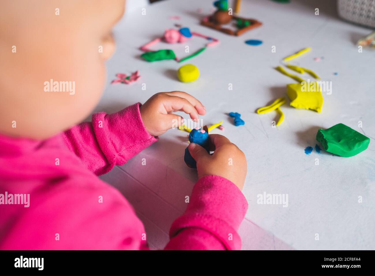 Dall'alto di vista irriconoscibile bambino che gioca con colorato modellare l'argilla su un tavolo bianco a casa Foto Stock