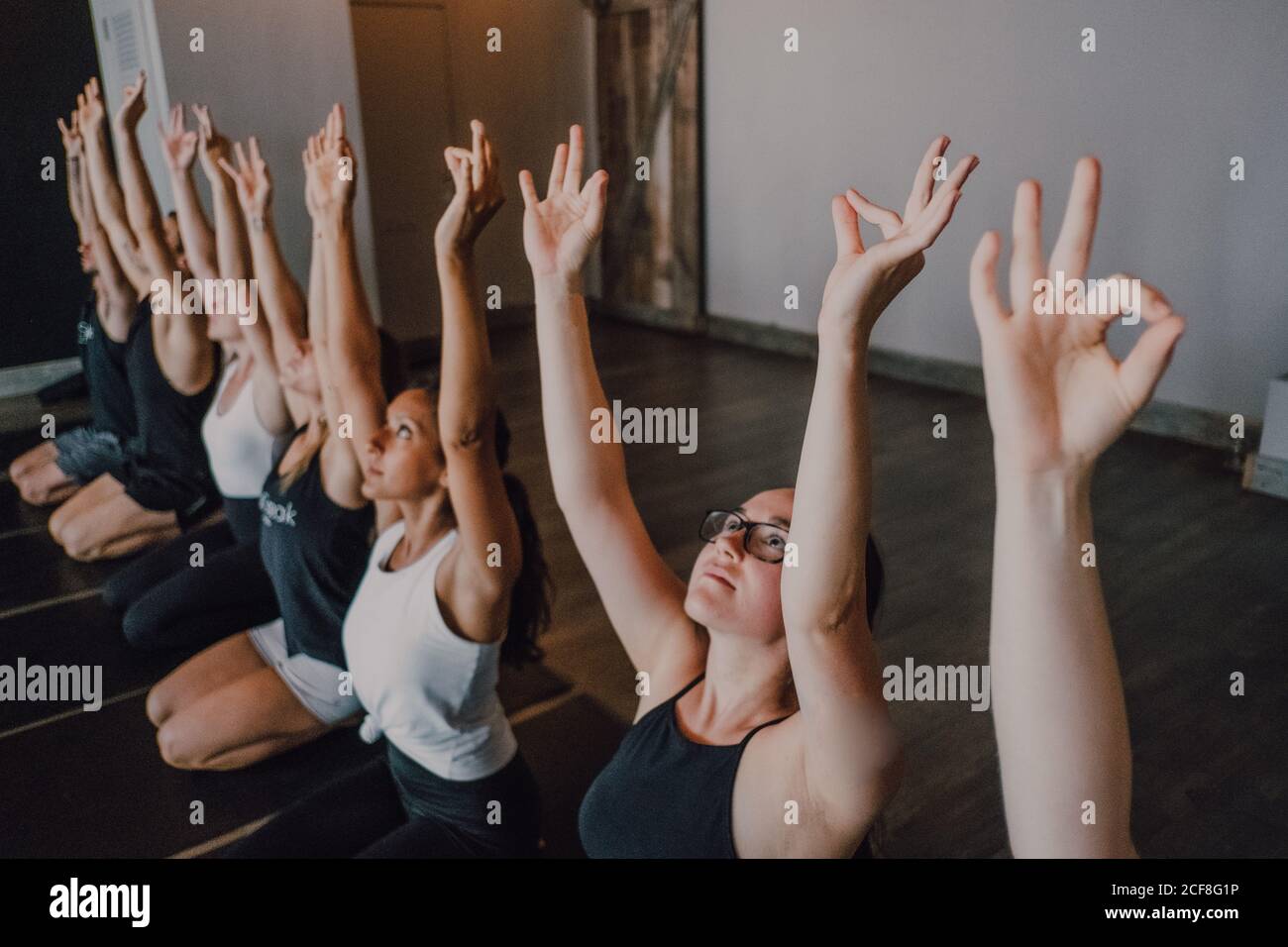 Alto angolo di gruppo di giovani donne e uomini sportivi In abbigliamento sportivo con braccia sollevate e corpo stretching Gyan Mudra e meditating mentre si siede in virasana posa su tappeti sportivi e cercando in su addestramento in studio di yoga moderno Foto Stock