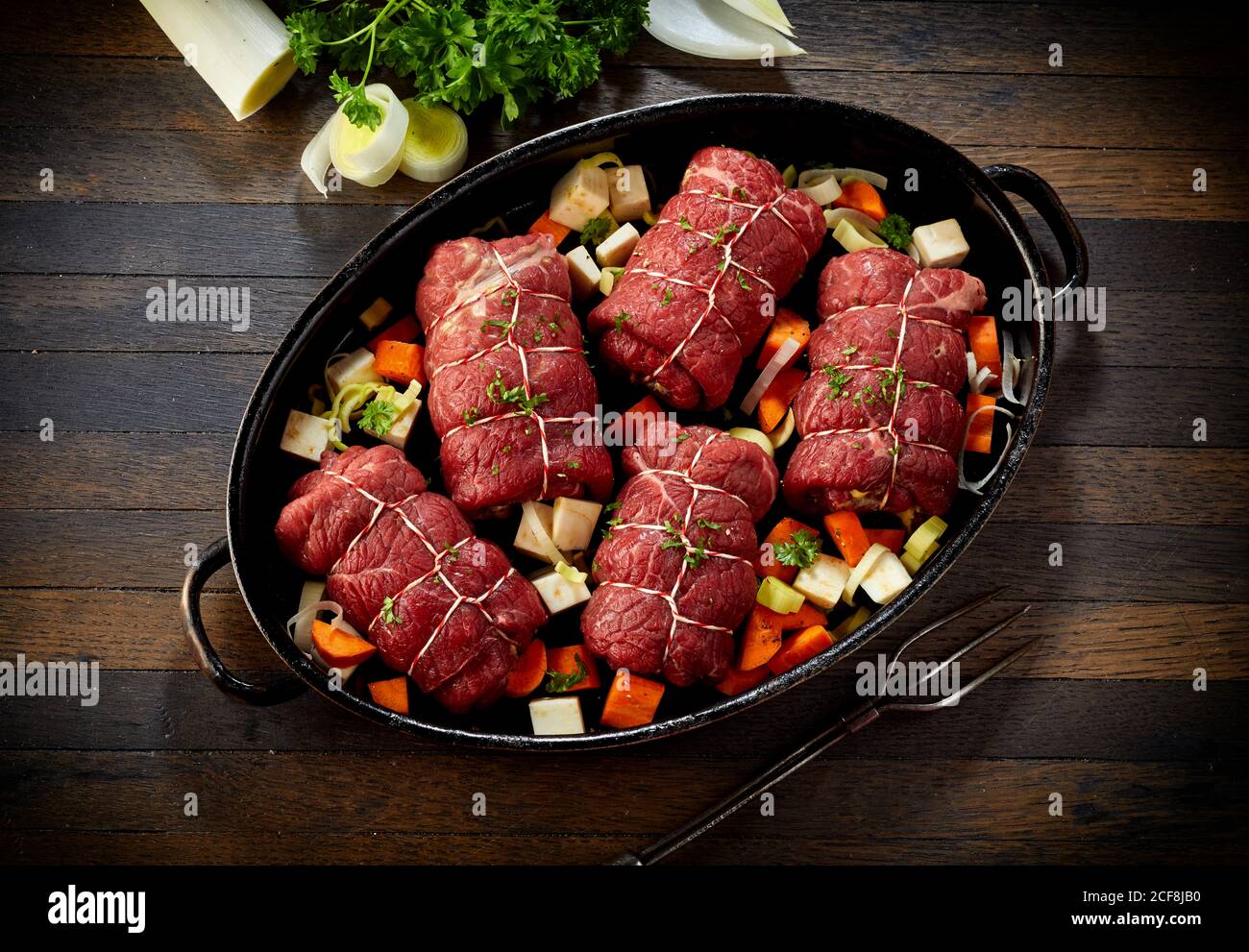 Preparazione di un tradizionale pasto tedesco di involtini di manzo in un piatto da forno con verdure fresche e stagionatura vista top down su un tavolo da cucina Foto Stock