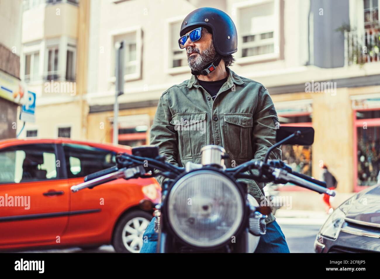 Uomo serio bearded in occhiali da sole e casco seduto su moto durante il  giro sulla strada della città guardando via Foto stock - Alamy