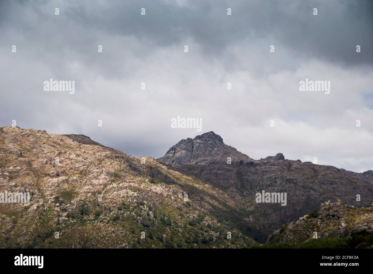 Vetta di montagna che mostra in lontananza, dietro più montagne e valli, ombreggiate da un cielo nuvoloso Foto Stock