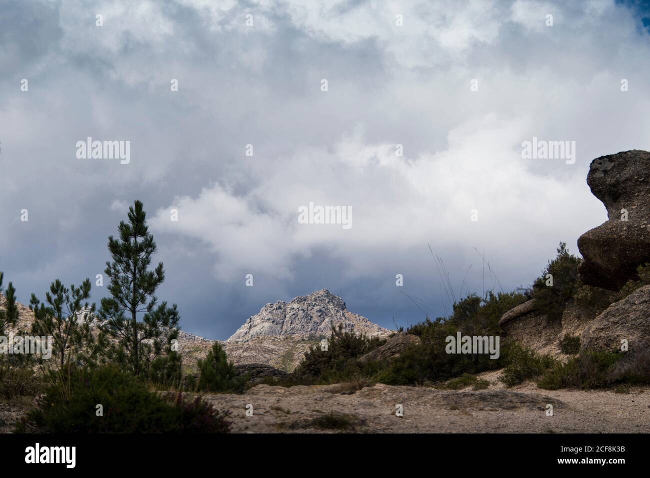 Vetta montana che mostra in lontananza, dietro un sentiero e più montagne e valli, ombreggiate da un cielo nuvoloso Foto Stock