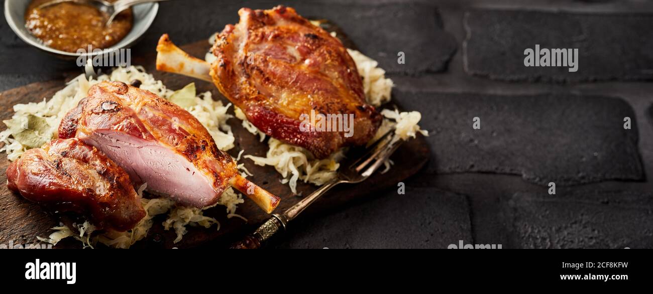 Due porzioni di Eisbein tedesco o prosciutti su crauti con una tagliata per mostrare la carne tenera un panorama con copyspace Foto Stock