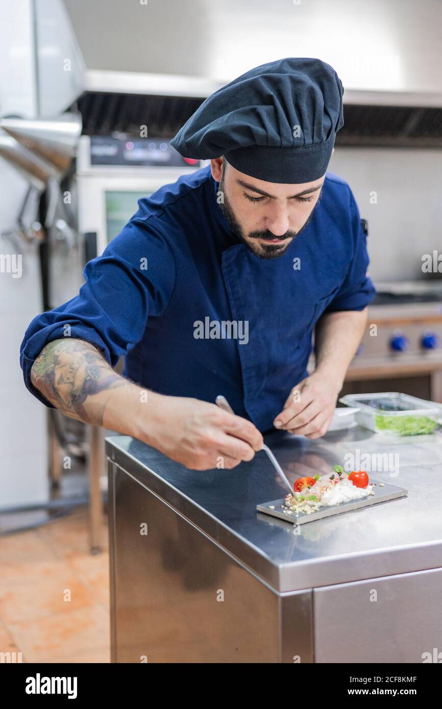 Concentrato professionista chef maschile guarnire e rifinire delizioso piatto pronto per servire mentre si lavora al banco metallico nella cucina del ristorante Foto Stock