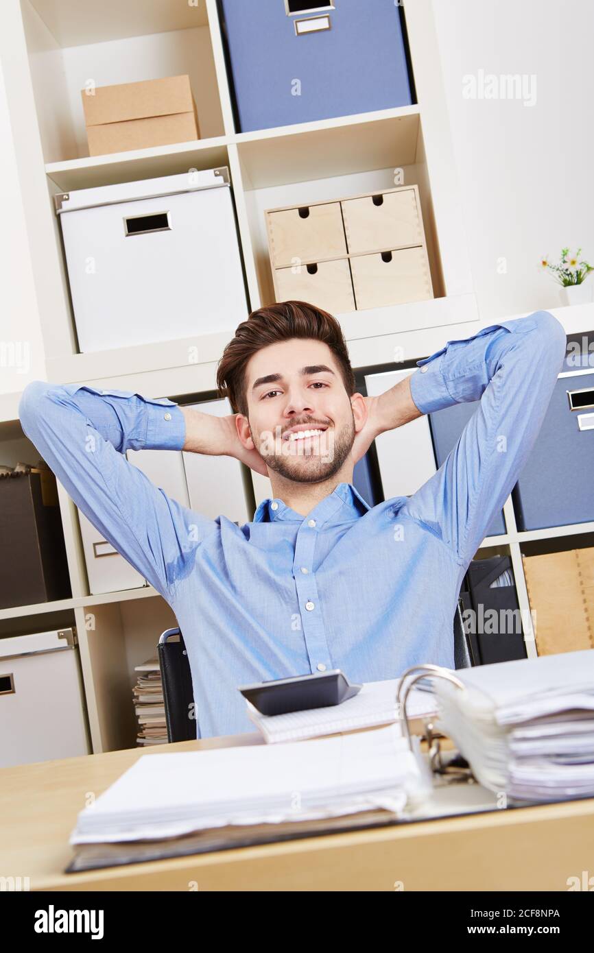 Un giovane di successo in ufficio si inclina a sorridere Foto Stock