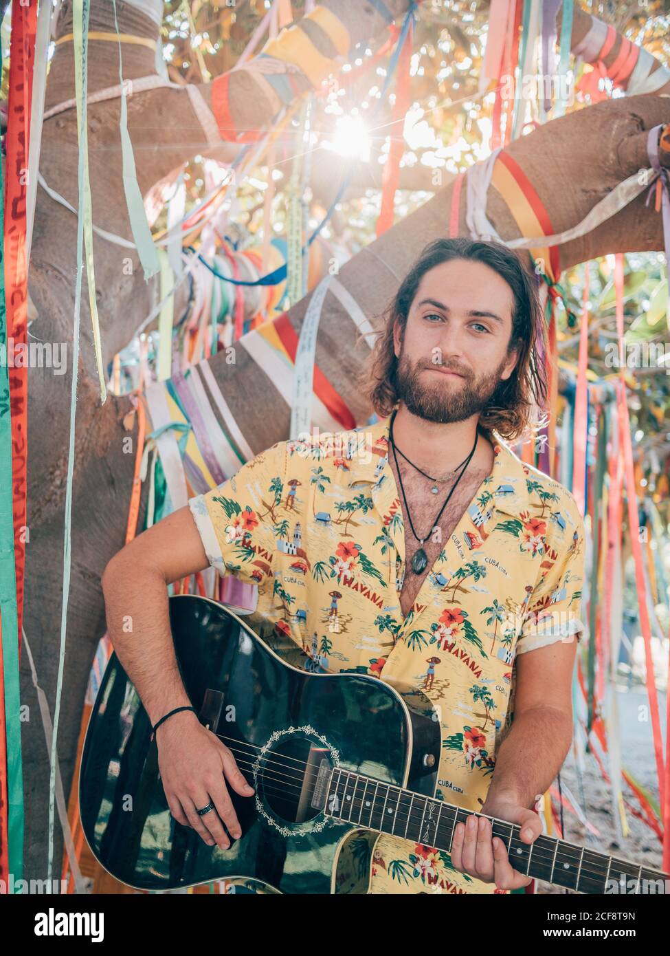 Uomo bearded seduto sotto albero decorato che suona la chitarra Foto Stock