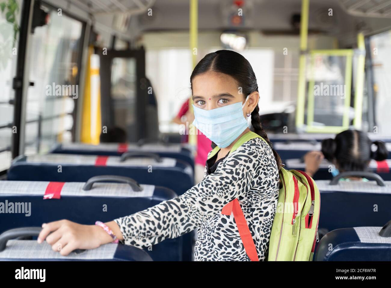 Ritratto di ragazza studente di capretto in maschera medica all'interno del Bus scolastico guardando la telecamera - concetto di riapertura scuola o di nuovo a scuola con nuovo normale Foto Stock