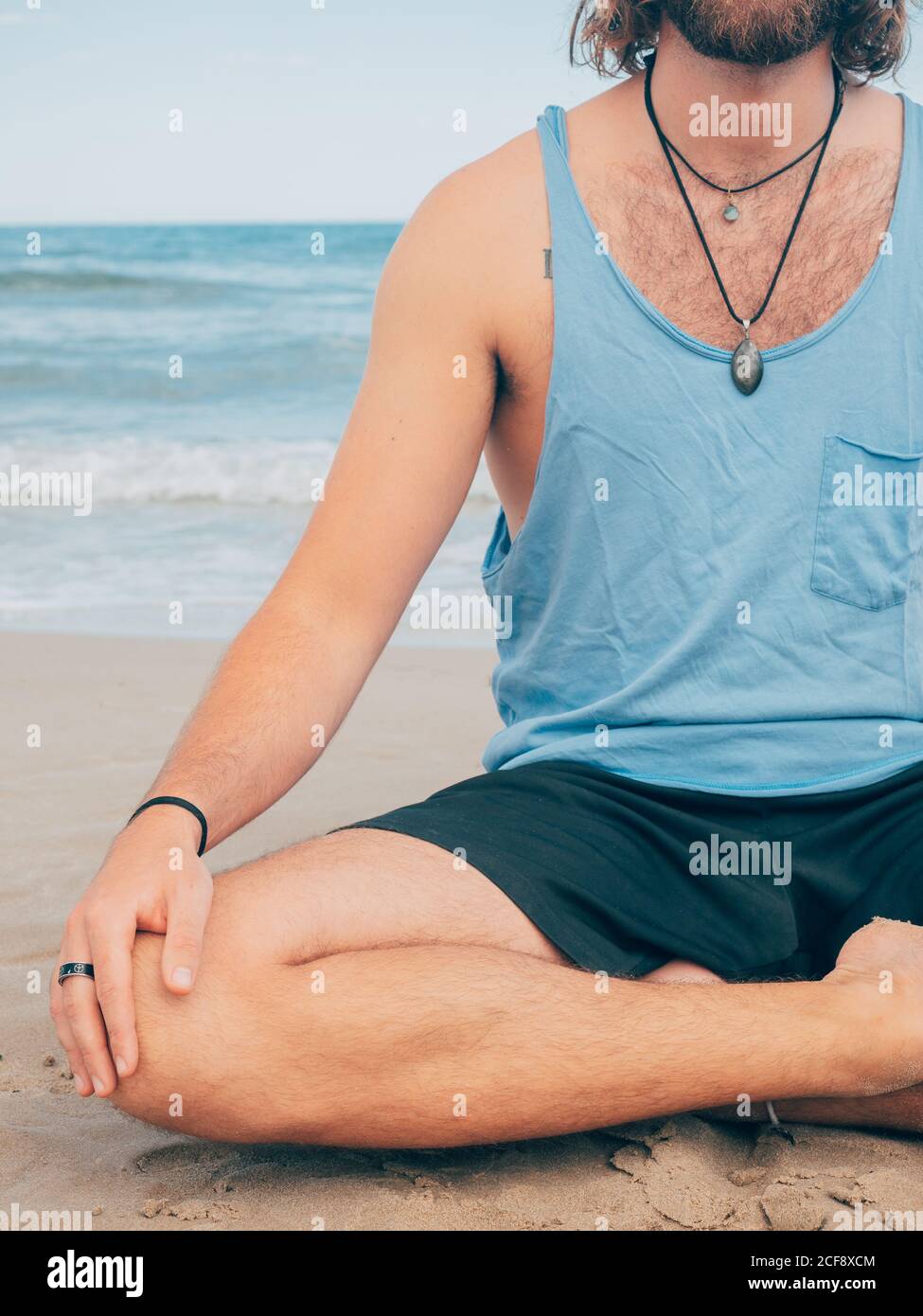 Crop irriconoscibile sportivo bearded maschile formazione su tranquilla mare e. fare yoga asana contro mare blu e cielo Foto Stock