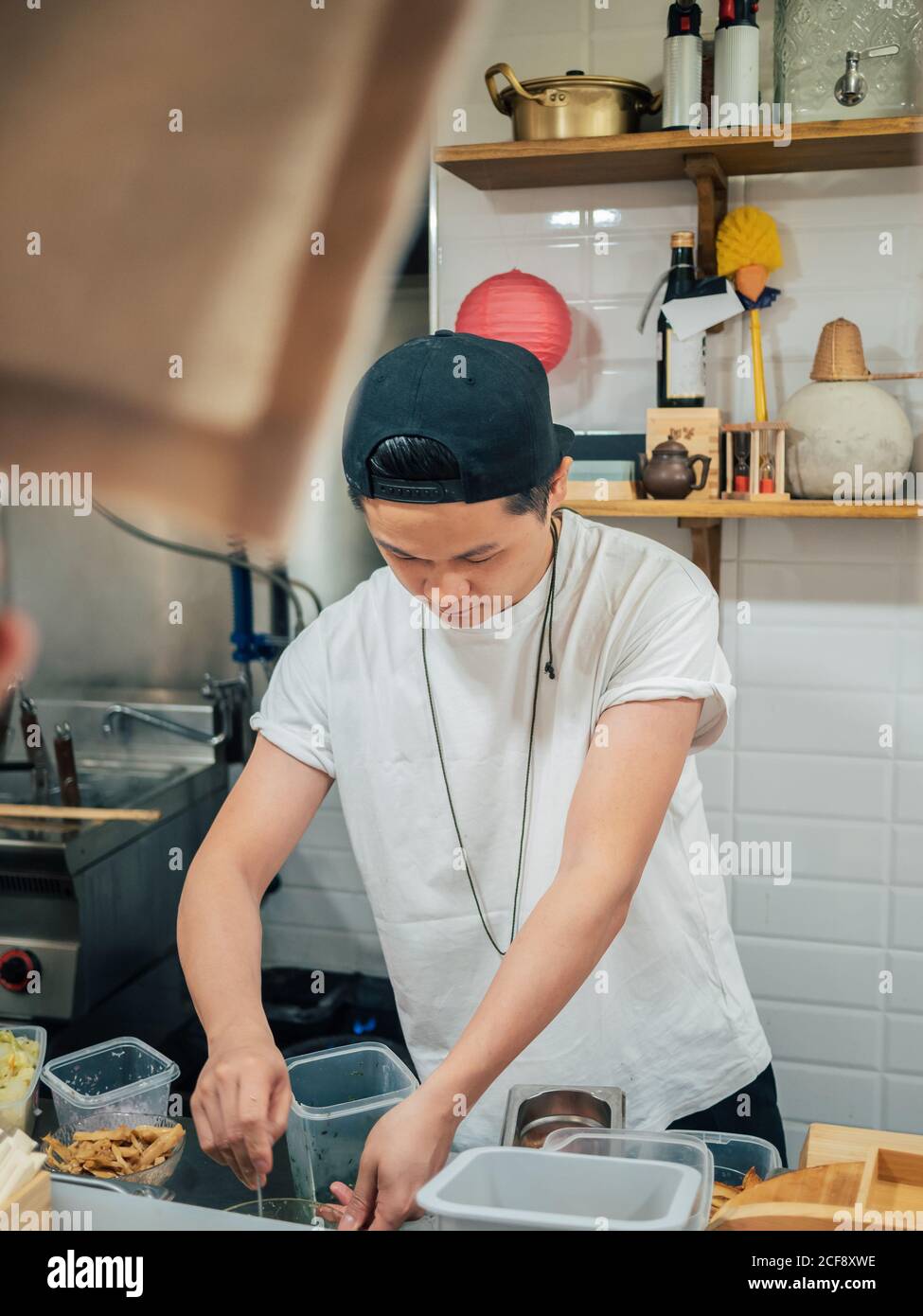 Giovane uomo in maglietta bianca e cappellino nero ramen cucina In ristorante giapponese Foto Stock