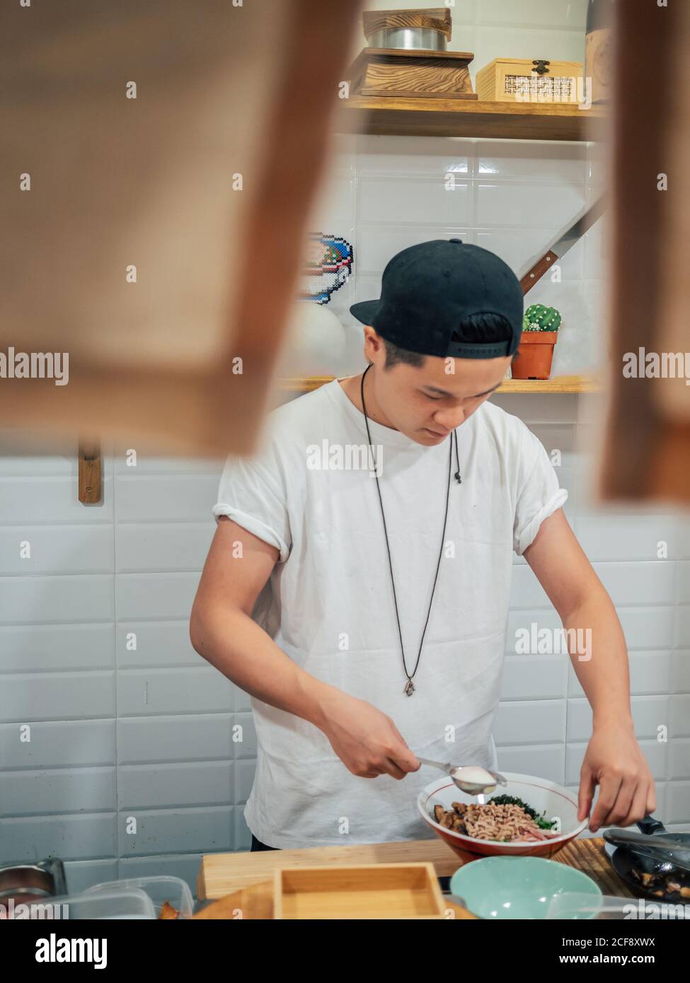 Giovane uomo in maglietta bianca e cappellino nero ramen cucina In ristorante giapponese Foto Stock