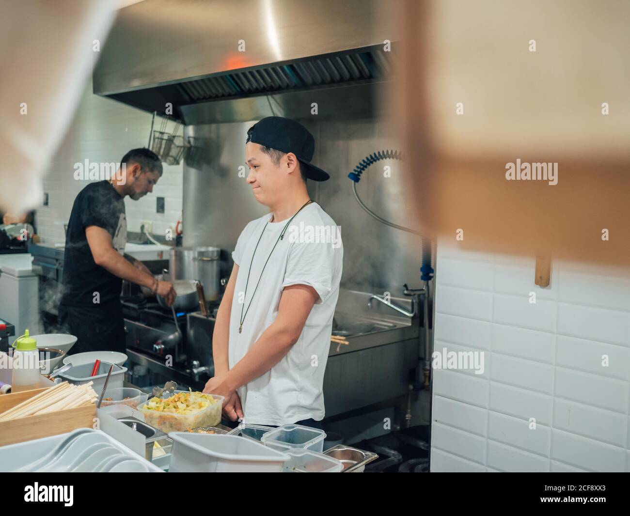 Giovane uomo in maglietta bianca e cappellino nero ramen cucina In ristorante giapponese Foto Stock