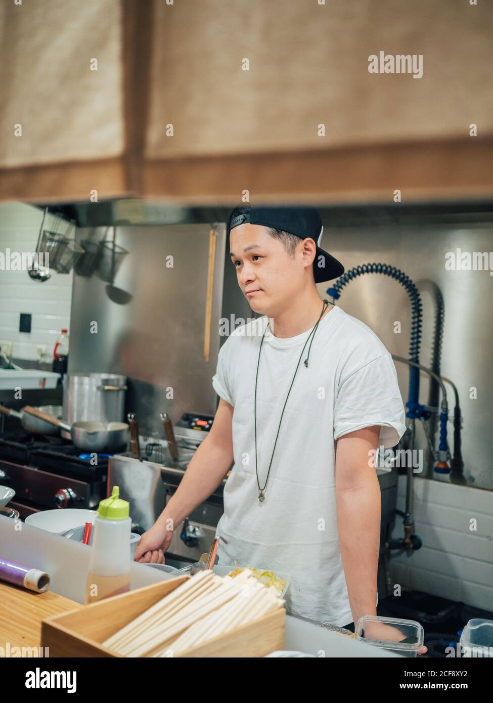 Giovane uomo in maglietta bianca e cappellino nero ramen cucina In ristorante giapponese Foto Stock