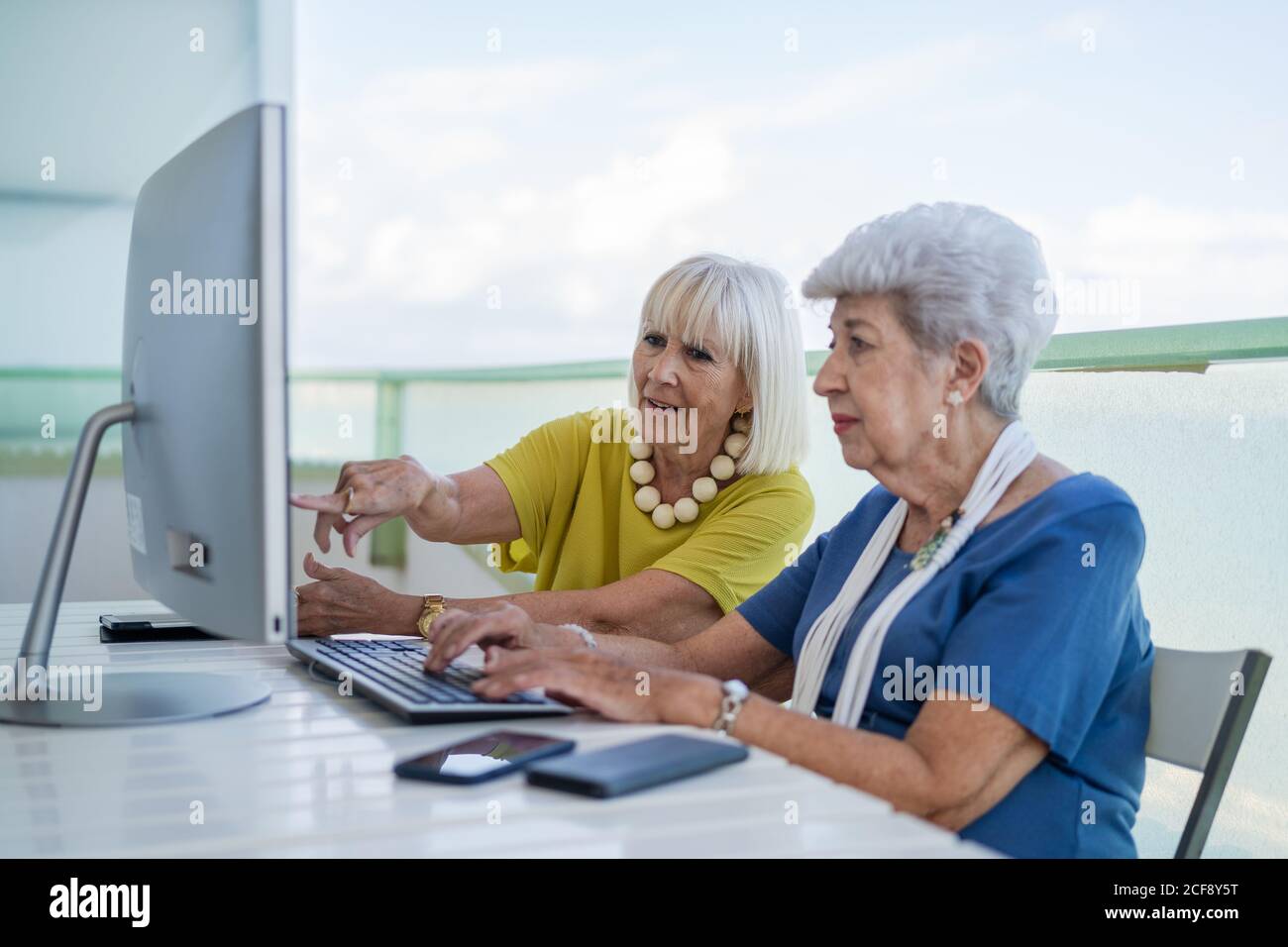 Eleganti vecchi amici seduti al tavolo con computer sul balcone sul resort Foto Stock