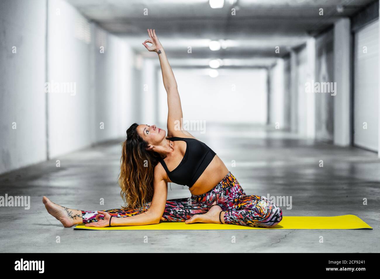 Vista laterale della donna adulta in rivoluzione testa a ginocchio posa mentre si pratica yoga in garage leggero sala guardando verso l'alto Foto Stock
