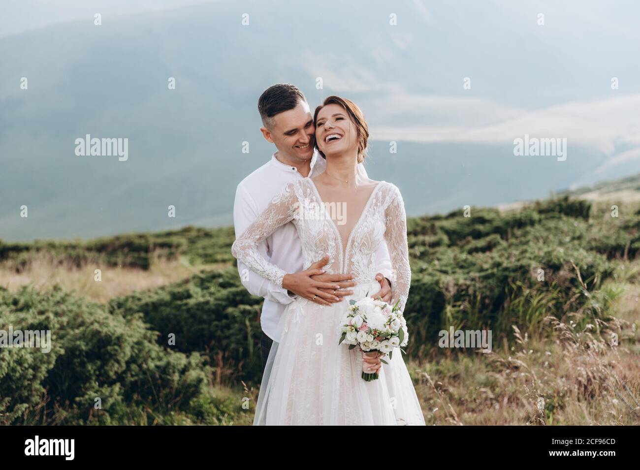 Felici sposi sorridenti, abbraccianti, che posano nei montani. Foto Stock