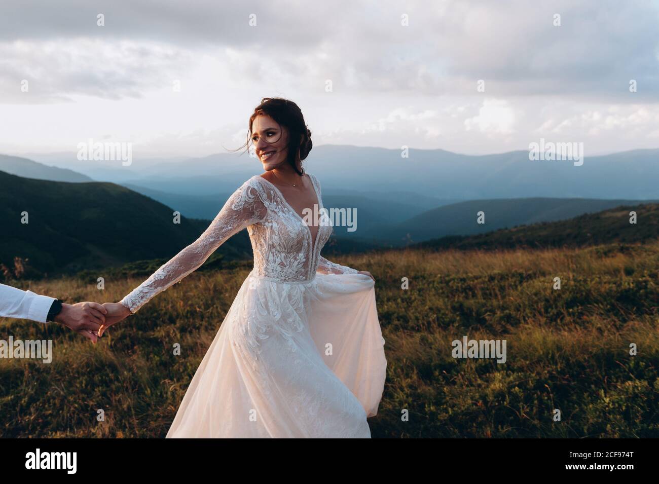 La sposa conduce lo sposo con la mano. Passeggiata di nozze in montagna al tramonto. Foto Stock