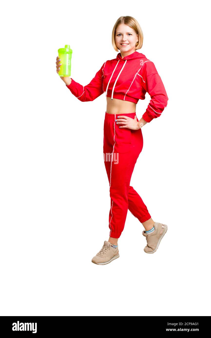 Una giovane donna felice in un vestito rosso di allenamento. Tenendo in mano una bottiglia d'acqua verde o uno shaker. Isolare su sfondo bianco. Foto Stock