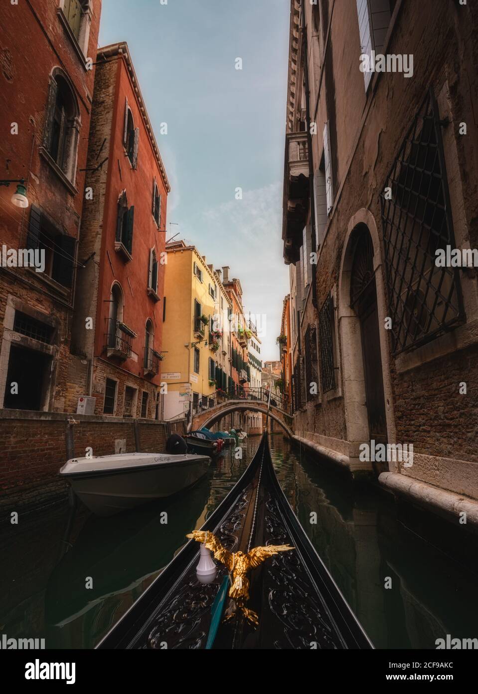 Becco ornamentale di gondola che galleggia lungo stretto canale con vecchio case di pietra sui lati Foto Stock